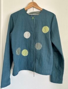 Handsydd blå jacka med runda dekorativa applikationer i gröna och vita toner på framsidan.”