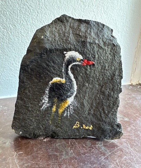 Målning av en häger med röd näbb, vit hals och gula inslag, målad direkt på en natursten.